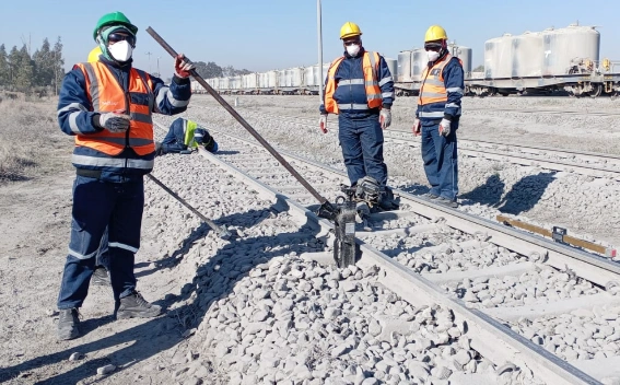 Workers in protective clothing working along ballasted railway track.