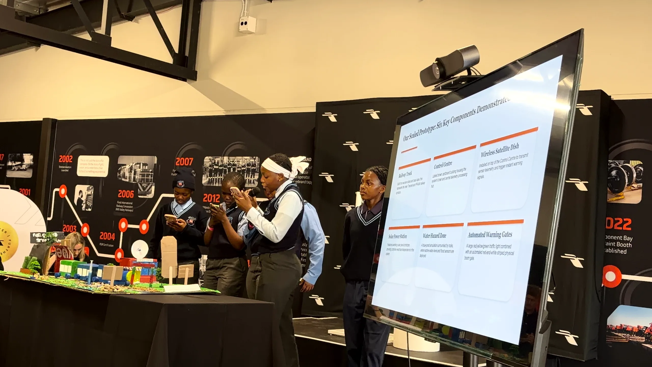 People presenting a model railway project beside a screen.